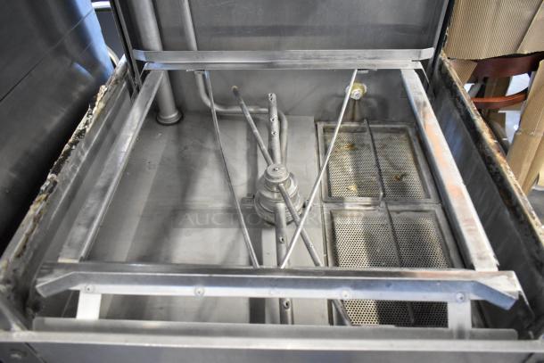 Commercial stainless steel dishwasher interior, showing spray arms and filters, in used condition. Visible wear on edges.