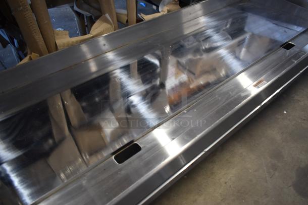 Stainless steel commercial display case, glass top, used condition, with visible scuffs and a small label on the side.