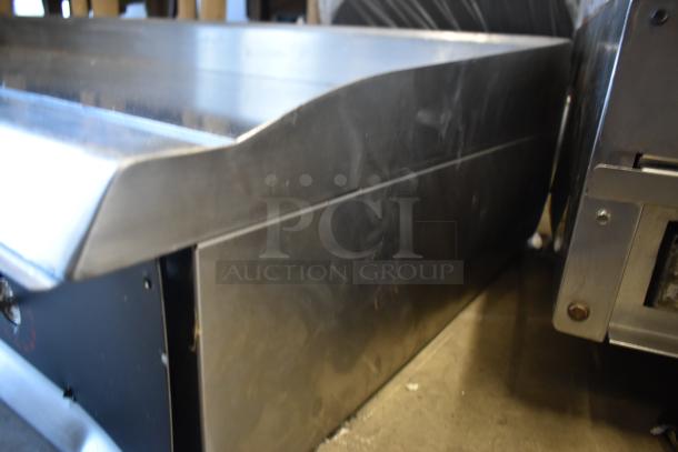 Stainless steel commercial conveyor oven, side view. Slight wear visible, suitable for high-volume food preparation.
