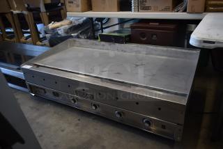 Vulcan commercial griddle with four control knobs, stainless steel surface, showing signs of use, model unidentified.