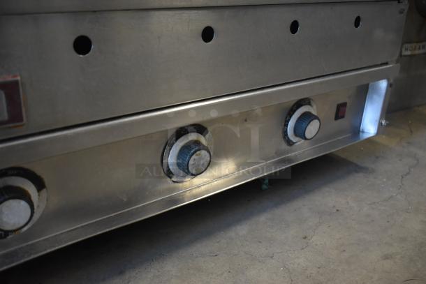 Stainless steel industrial oven with three control knobs and a power switch, showing signs of use.