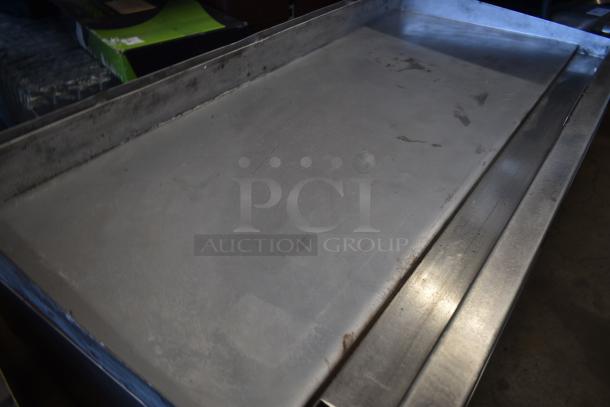 Stainless steel flat griddle with raised edges, some surface wear, suitable for commercial kitchen use.