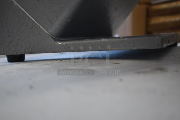 Close-up of the base of a gray industrial machine with a textured, worn finish on a concrete surface.