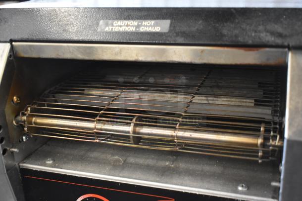 Commercial toaster with metallic heating elements, showing signs of use. "Caution - Hot" label is visible.