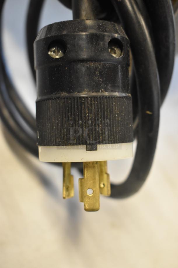 Close-up of a black electrical plug with brass prongs, showing signs of wear, suitable for heavy-duty electrical use.