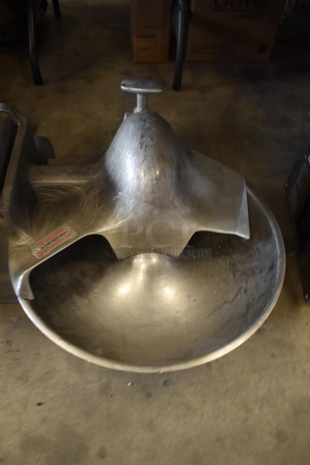 Industrial metal mixing bowl with a safety label, showing wear; large, curved design for food processing equipment.