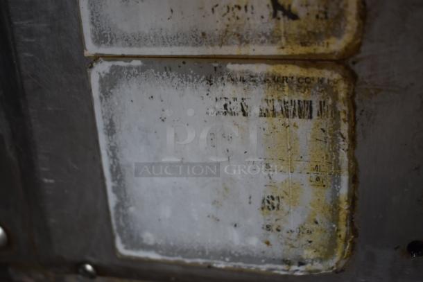 Close-up of a metal surface with worn, partially visible labels showing unclear text and markings, indicating age and use.