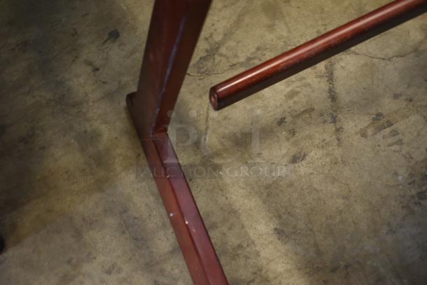 Red metal furniture leg on concrete floor, showing minor wear and scratches, indicating used condition.