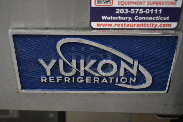 Close-up of Yukon Refrigeration logo on a metallic surface, showing some wear. Above is a label from a restaurant equipment store in Waterbury, Connecticut.