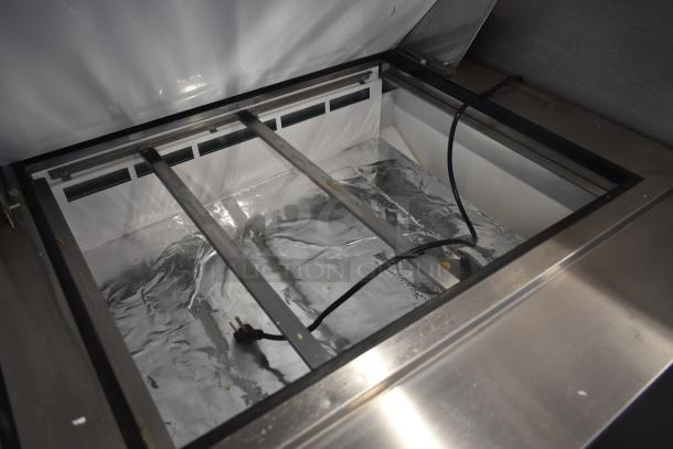 Commercial stainless steel refrigerated prep table with open lid, showing an interior cooling compartment. Visible clean surface and intact electrical cord, indicating good condition. Ideal for food service use.