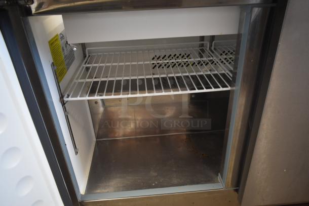 Commercial stainless steel refrigerator interior with wire shelf, clean condition, visible safety and usage labels.