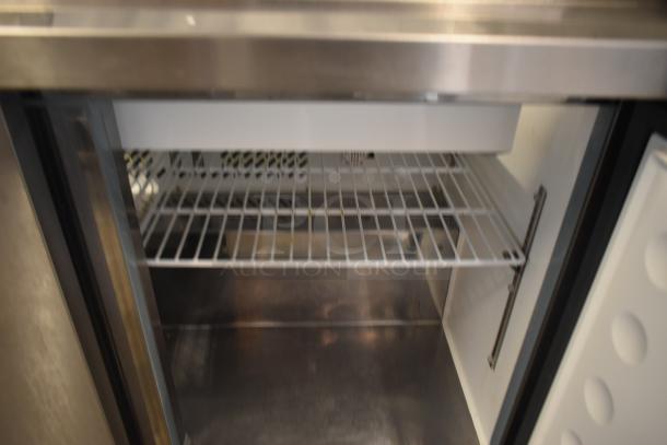 Stainless steel under-counter refrigerator, open door, showing wire shelf and clean interior. Ideal for compact storage.