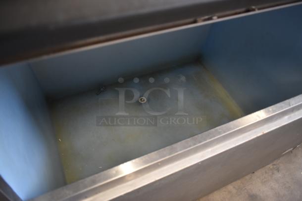 Stainless steel commercial ice bin, open top view, showing drain at the bottom, some discoloration, and a few scattered screws inside.