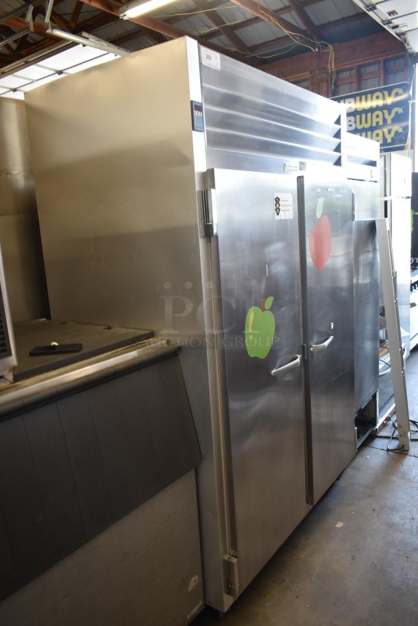 Commercial stainless steel refrigerator/freezer with double doors, apple decals, and minor surface wear.