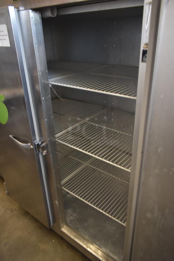 Stainless steel commercial refrigerator, four shelves, open door, signs of wear, suitable for food storage.