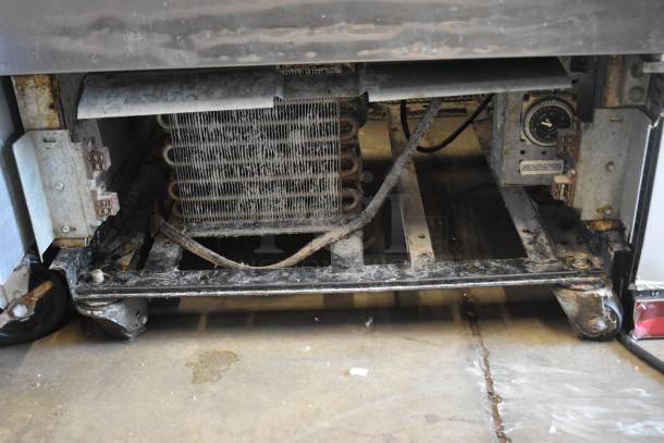 Industrial refrigeration unit base, showing exposed coils and components. Signs of wear and dust accumulation.