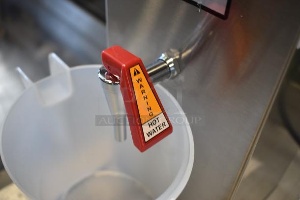 Commercial hot water dispenser with red warning handle, marked "Warning Hot Water," mounted on stainless steel.
