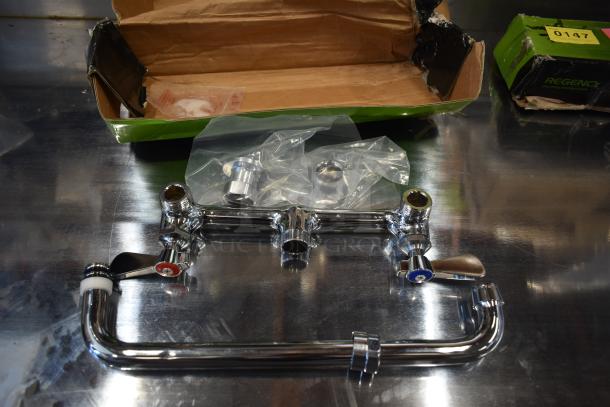 Chrome faucet assembly with hot and cold handles, new in open box, includes installation parts in plastic bags, Regency brand visible.