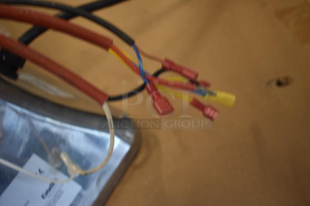 Electrical wiring bundle with red connectors and mixed colored wires; attached to a metallic base with visible label.