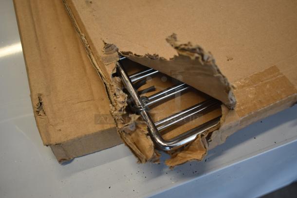 Damaged cardboard box revealing chrome metal rack, condition unknown, with packaging wear.