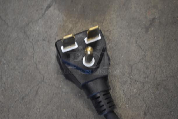 Black electrical plug with three gold prongs on concrete surface, showing slight wear. 