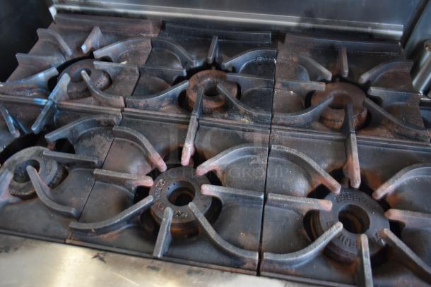 Commercial six-burner gas stove, cast iron grates, used condition with visible wear and rust.