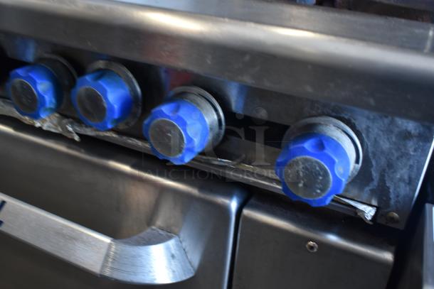 Commercial stainless steel stove with four blue control knobs, showing signs of wear. Ideal for professional kitchens.