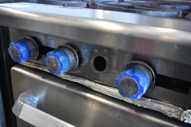 Commercial stainless steel stove with blue control knobs, showing signs of use. Scratches and wear visible on surface.