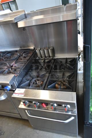 Commercial stainless steel gas stove with six burners and control knobs, showing signs of use. Auction lot tag number 293 attached.