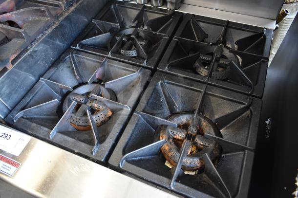Commercial gas stovetop with four burners, showing signs of rust and wear. Auction label indicates item number 293.