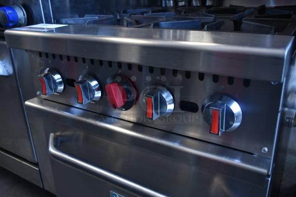 Commercial stainless steel gas stove, five control knobs, includes oven handle. Good condition, ideal for professional kitchens.