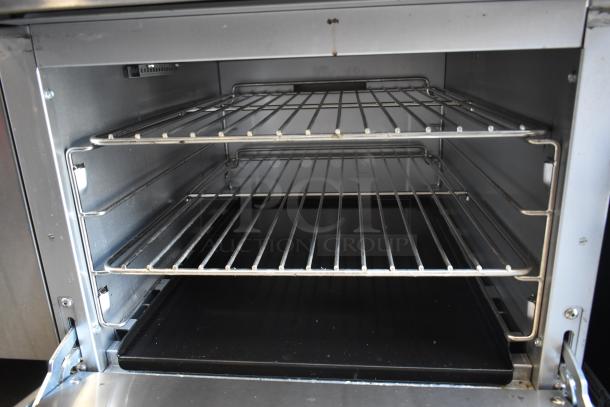 Stainless steel oven interior with two wire racks and a removable black tray, in good condition, showing a clean and spacious design.