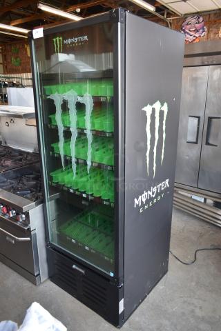 Monster Energy branded beverage cooler with glass door, green shelving, and logo graphics. Black exterior, good condition.