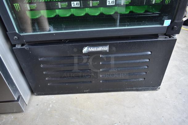 Metalfrio beverage cooler base with visible drinks on top shelf. Black exterior with vented front panel and brand label.