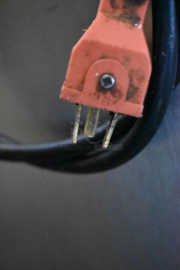 Close-up of an orange electrical plug with two metal prongs and a black cable. The plug shows signs of wear and discoloration.