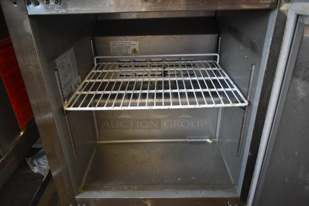 Commercial stainless steel warming cabinet with a single wire shelf, showing moderate wear. Safety labels and temperature settings visible.