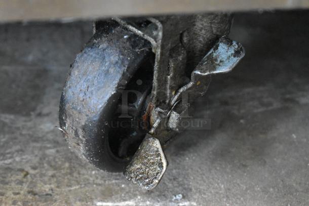 Rusty industrial caster wheel showing wear, with a metal bracket attached. Surface appears dirty, indicating heavy use.