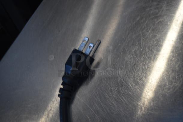 Black electrical power plug on a scratched metal surface, showing two metal prongs.