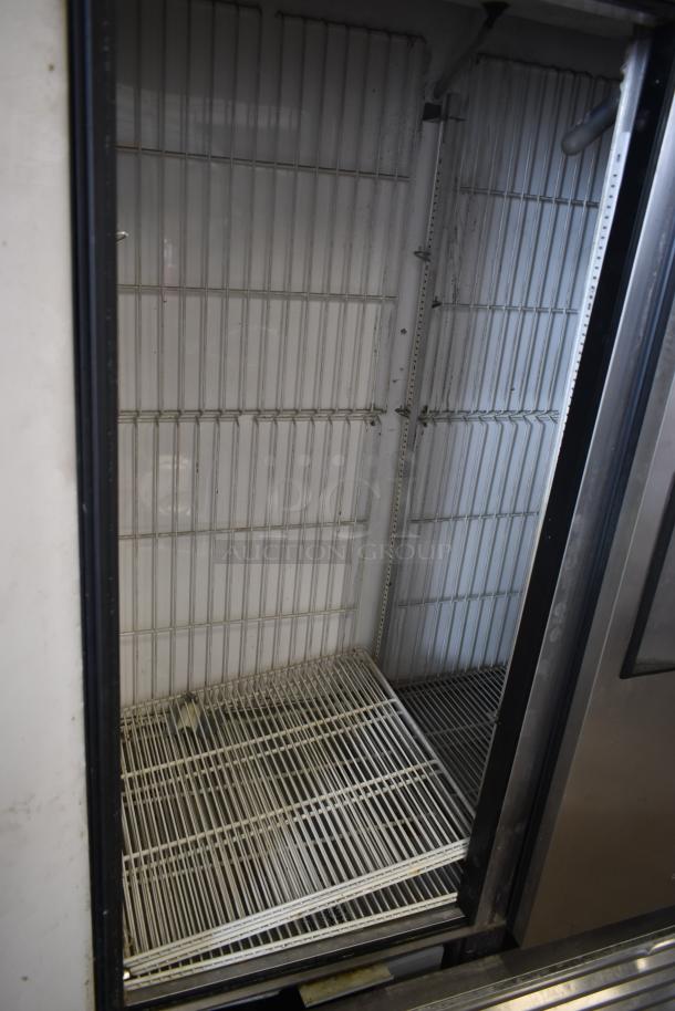 Commercial stainless steel refrigerator interior with empty wire shelves, showing signs of use and slight discoloration.