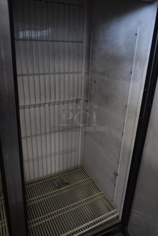 Commercial refrigerator interior with metal shelves, visible wear, and scratches. Empty and clean with a dim interior light.