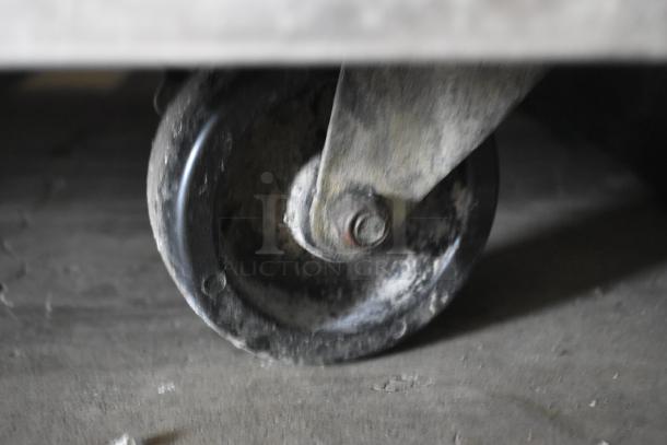 Rustic industrial caster wheel, showing signs of wear and aging, made of metal with a swivel mount.