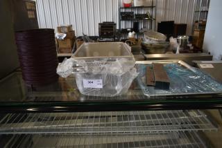Stack of round baking pans, stainless steel trays, and metal containers on display. Auction tag reads "Lot 304."