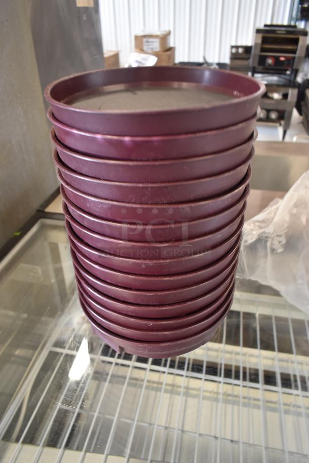 Stack of burgundy plastic trays, used condition, showing minor wear. Suitable for food service or catering use.