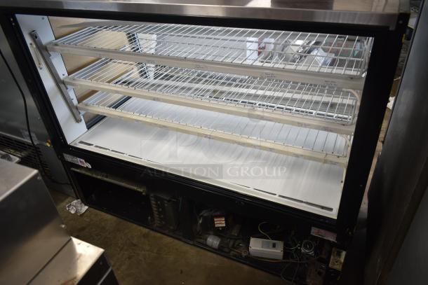 Commercial refrigerated display case with four adjustable wire shelves, stainless steel exterior, visible wiring below, fair condition.