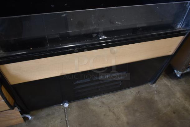 Black and wood commercial display case with glass top, minor wear, ventilation panel at the base, suitable for retail use.