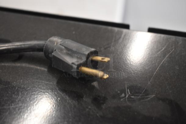 Black two-prong electrical plug with visible wear on a glossy surface.