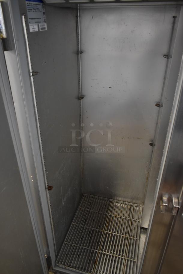 Commercial stainless steel freezer interior with shelving. Visible wear and use; inspection tag in corner indicates model details.