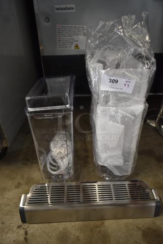 Clear plastic container with measurements, wrapped item with auction label "309 QTY X3," and metal grill part, on a floor.