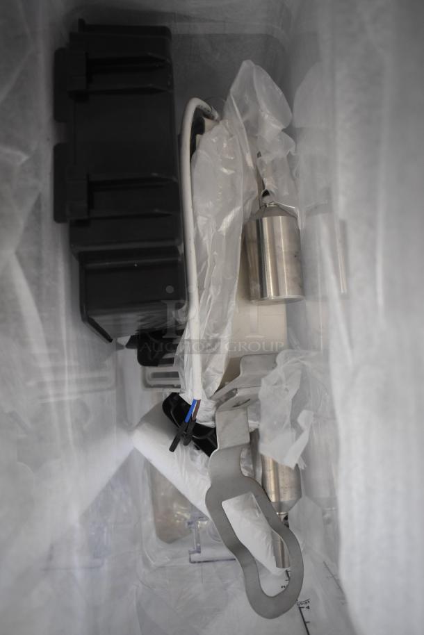 Box of assorted metal and plastic parts, including a large black component and a wrapped cylindrical silver piece. Appears unused.