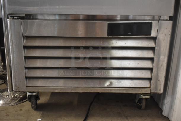 Commercial stainless steel freezer with vented front, mounted on wheels. Visible wear indicates moderate use. No labels visible.